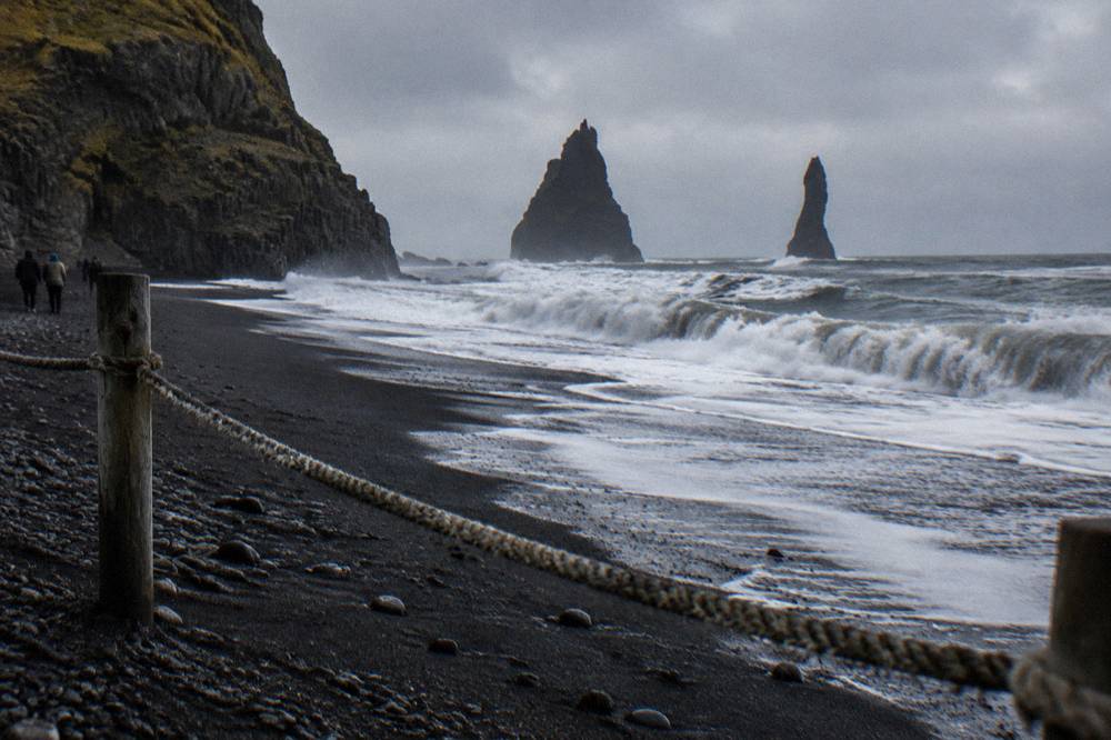 Dark waves breaking on black sand with a rope and warning signpost in the foreground