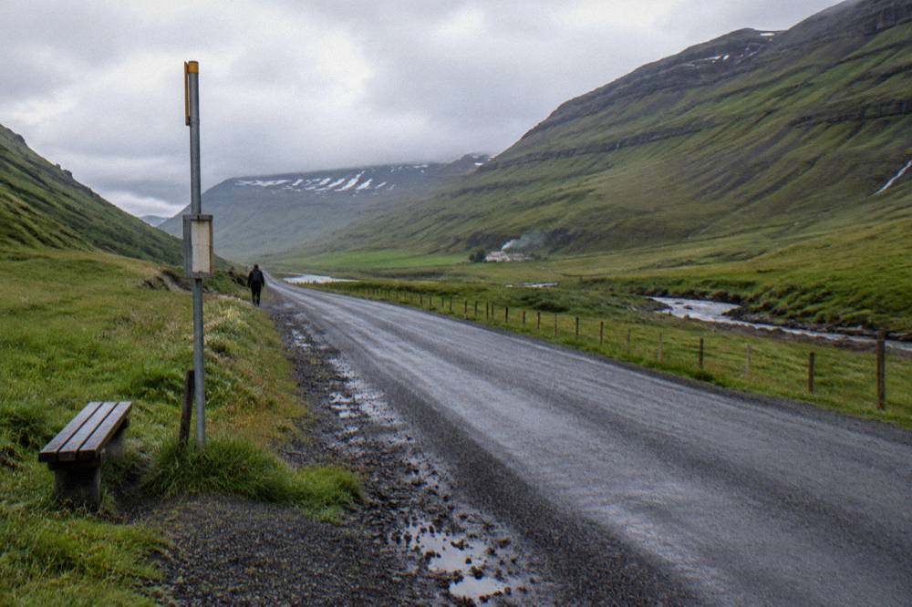 A country road in Iceland with a bus stop sign and green hills behind it