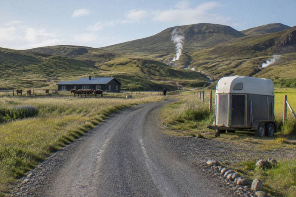 A country road winding through farmland with mountains in the distance