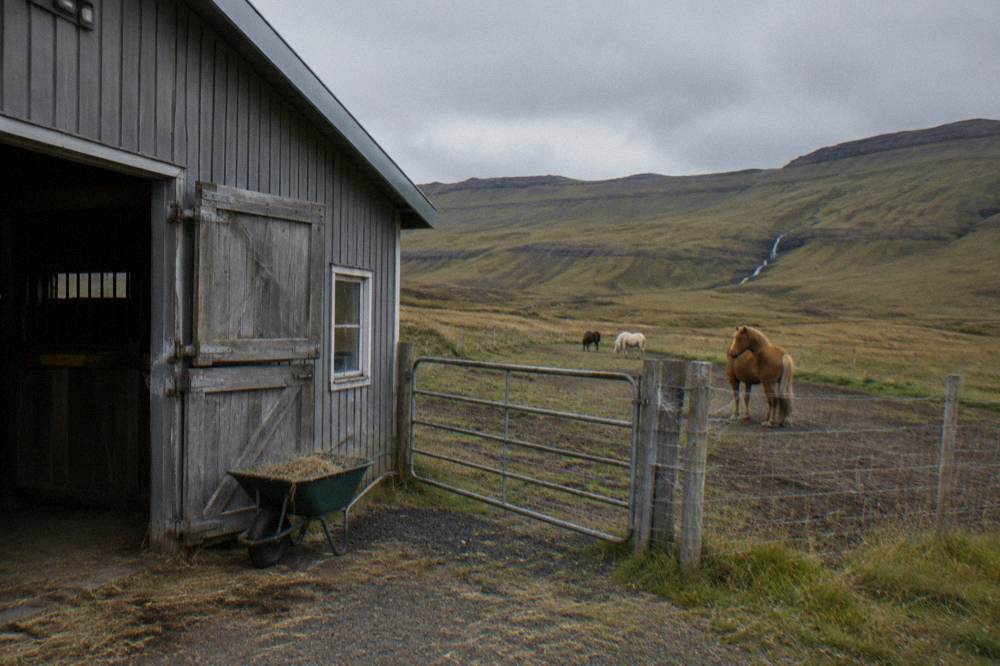 A wooden stable barn beside a paddock with hills behind
