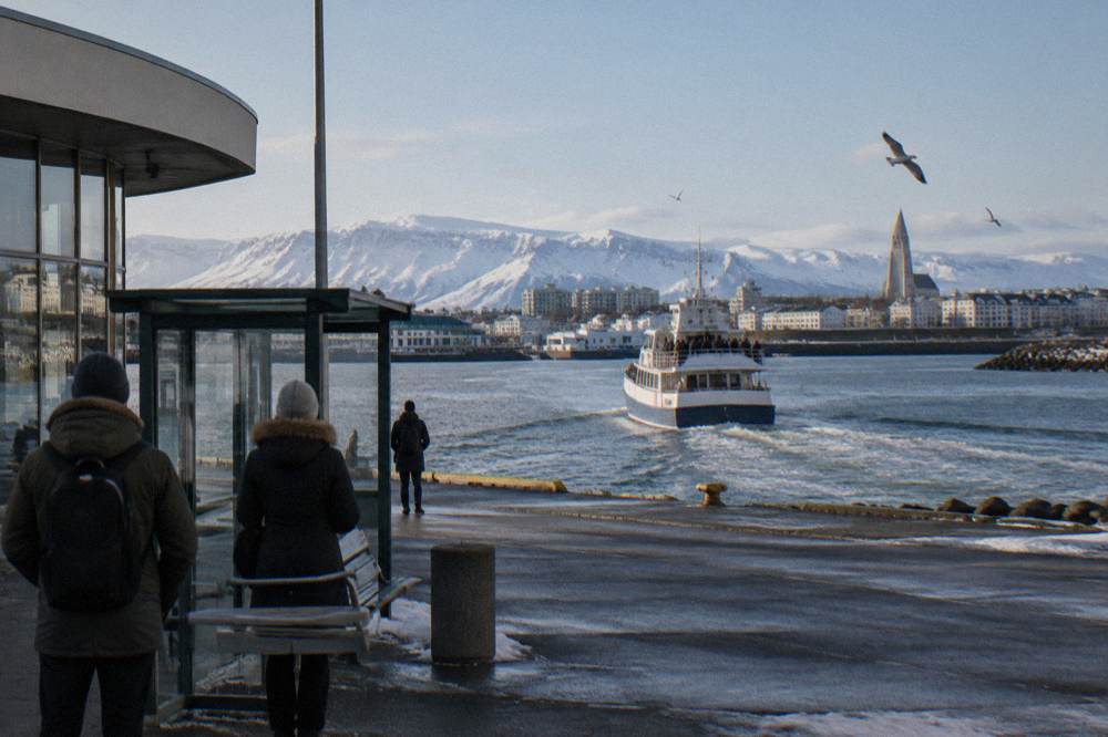 A whale watching boat leaving Reykjavik old harbour with snow capped mountains behind