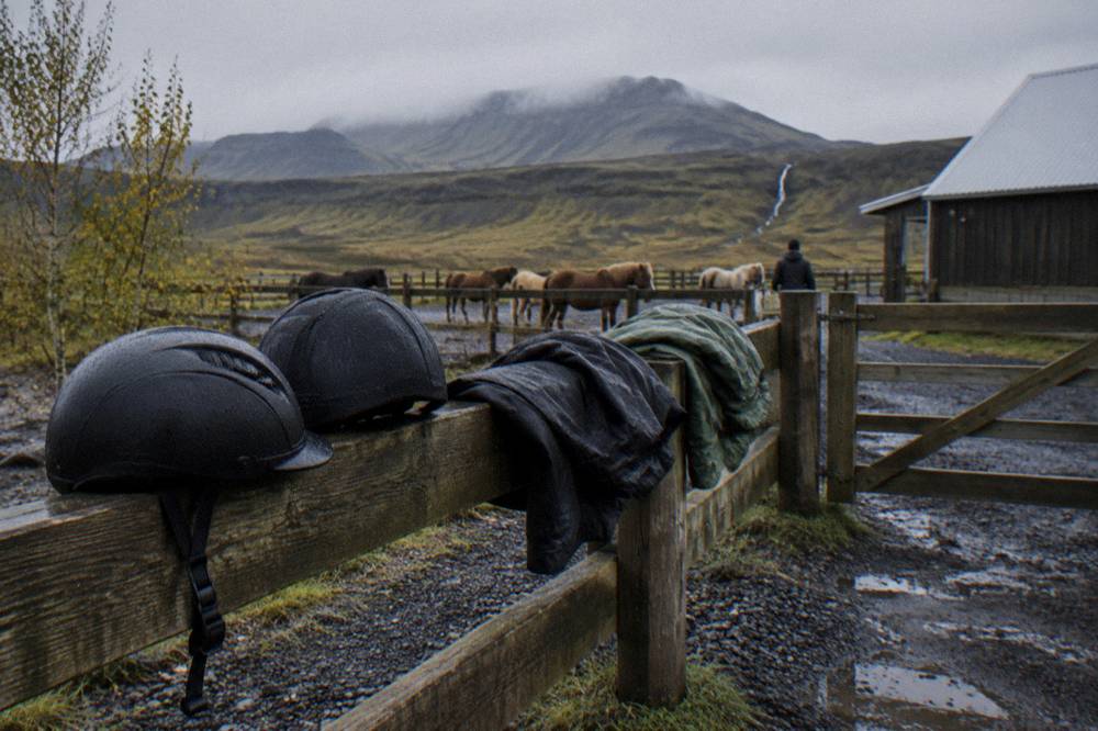 Riding helmets and waterproof jackets laid out on a stable fence before a tour