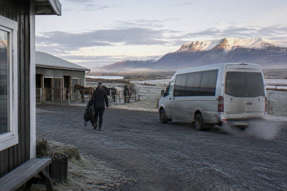 A small bus parked on a gravel lane beside a horse stable in southwest Iceland