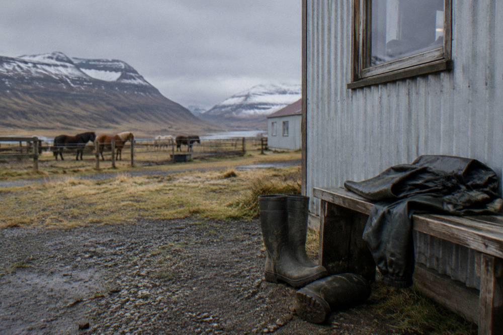 Rubber boots and rain gear arranged on a bench outside an Icelandic stable building