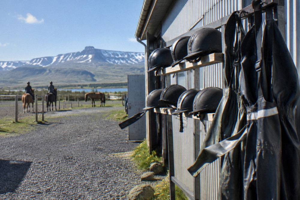 A rack of riding helmets and hanging rain overalls outside an Icelandic stable building