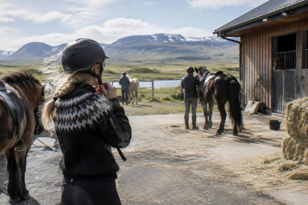 Riders fitting helmets beside a stable yard before a lava field ride
