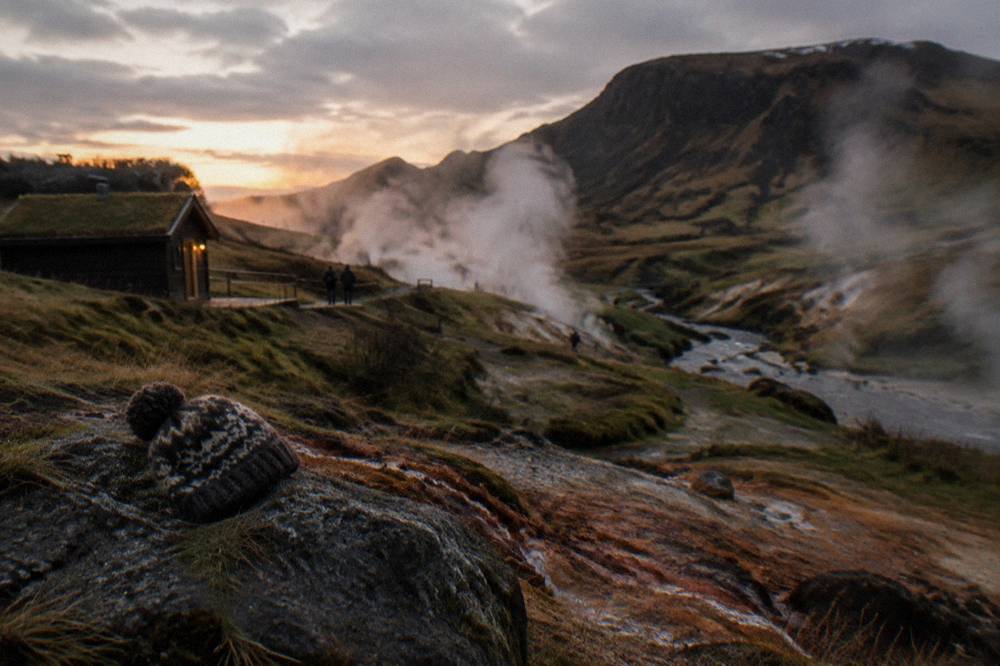 Steam rising from geothermal hillsides above a dark valley at dusk