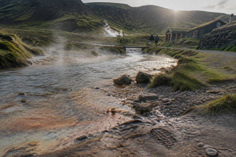 Steam rising from hot streams in a green valley below mossy hills