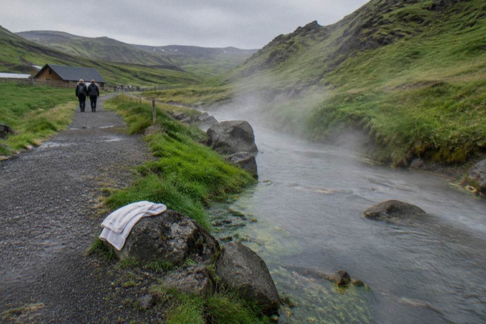 A shallow hot river steaming beside a gravel trail in a valley