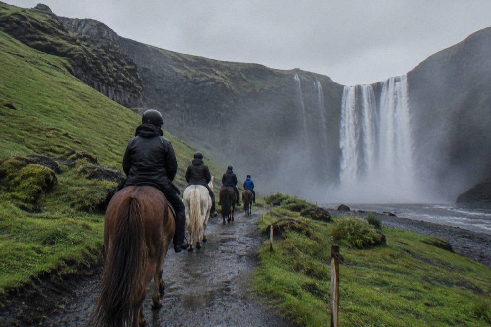 A small group of riders on Icelandic horses along a trail near a waterfall