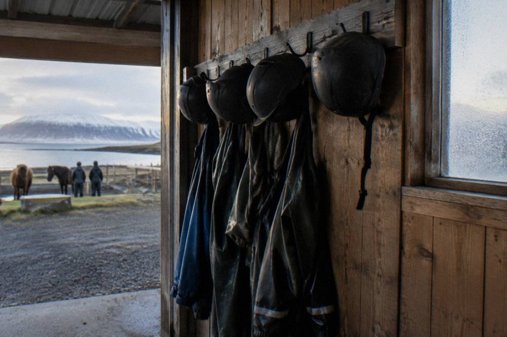 Rack of helmets and rain overalls hanging on a stable wall
